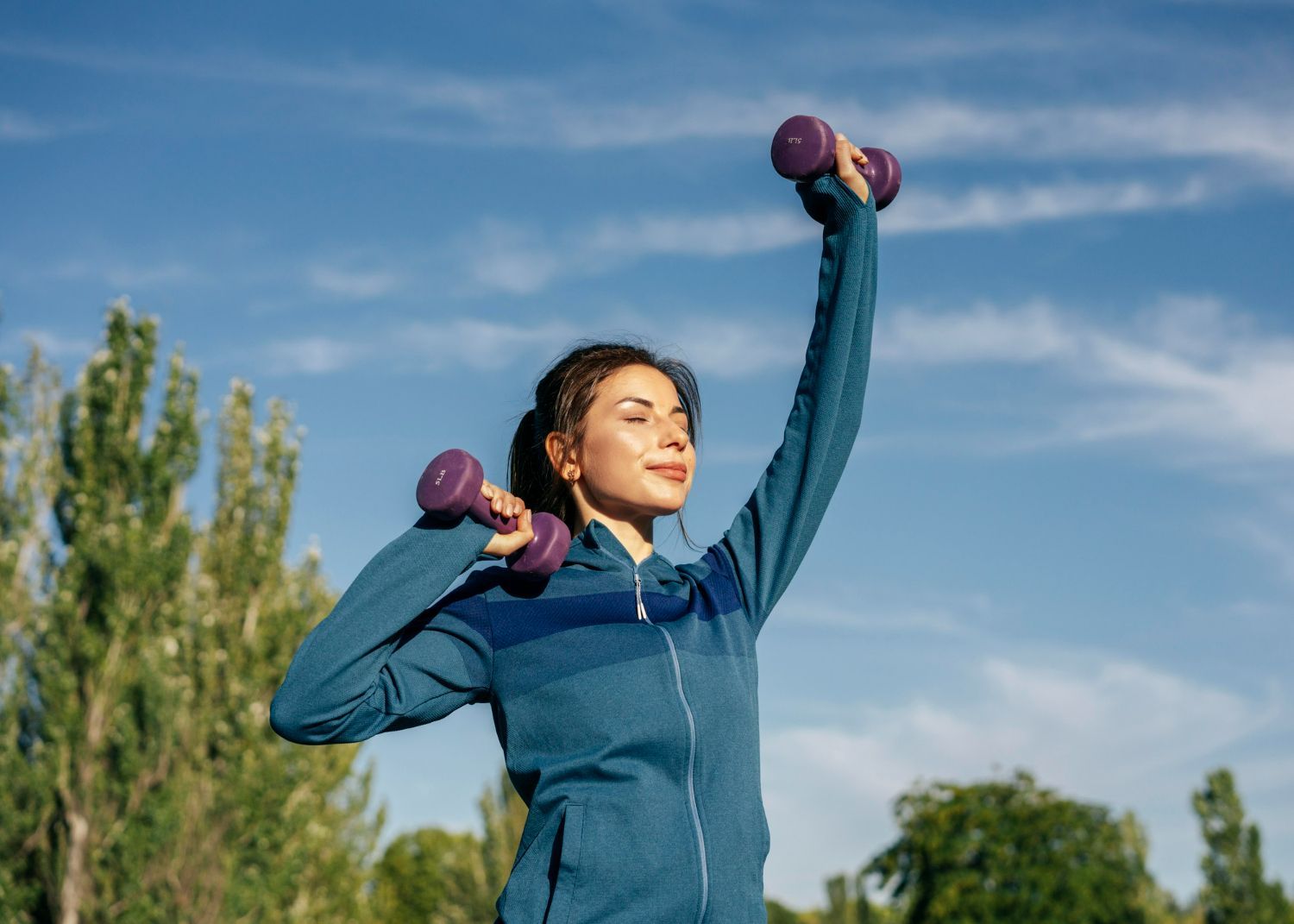 A woman is lifting dumbbells in a park.