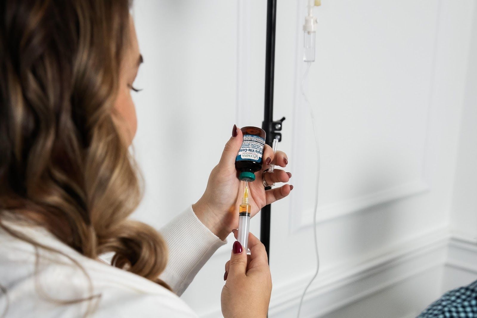 Woman filling syringe from a vial, IV drip stand in background.