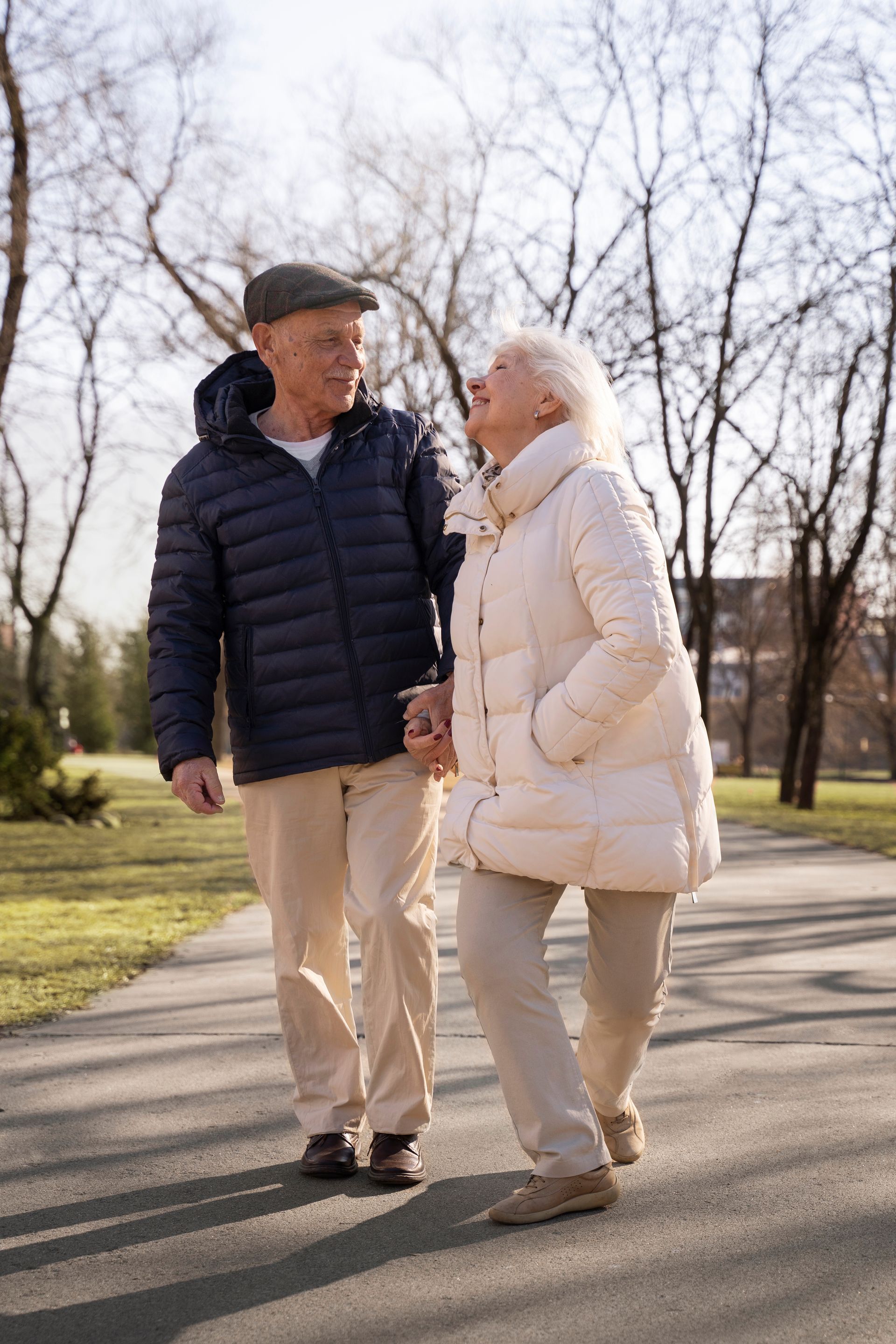 An elderly couple is walking down a path in a park holding hands.