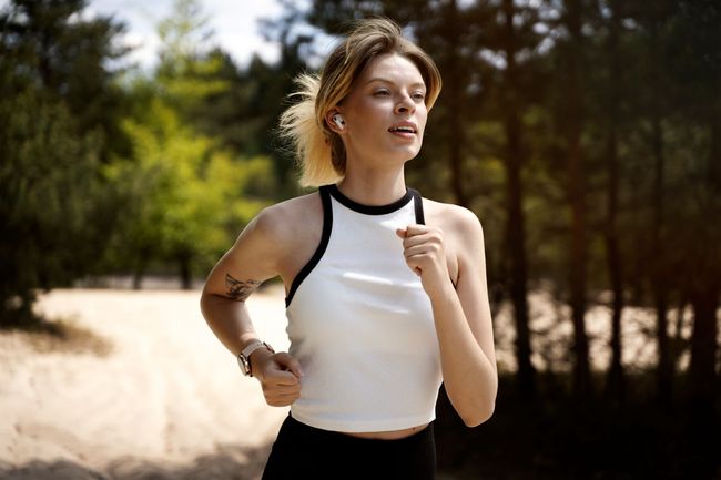 A woman in a white tank top and black pants is running in the woods.