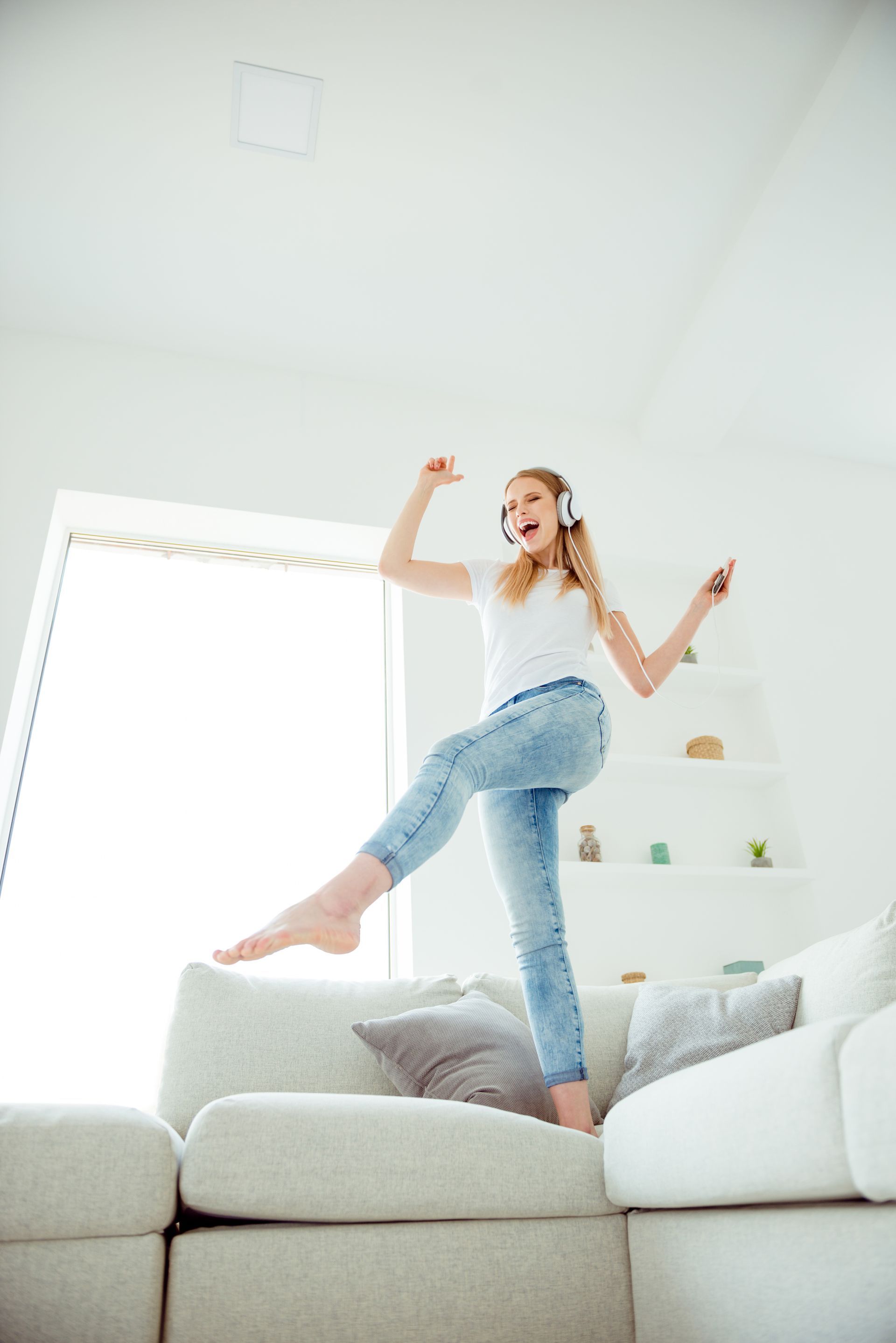 A young girl is jumping on a couch while listening to music.