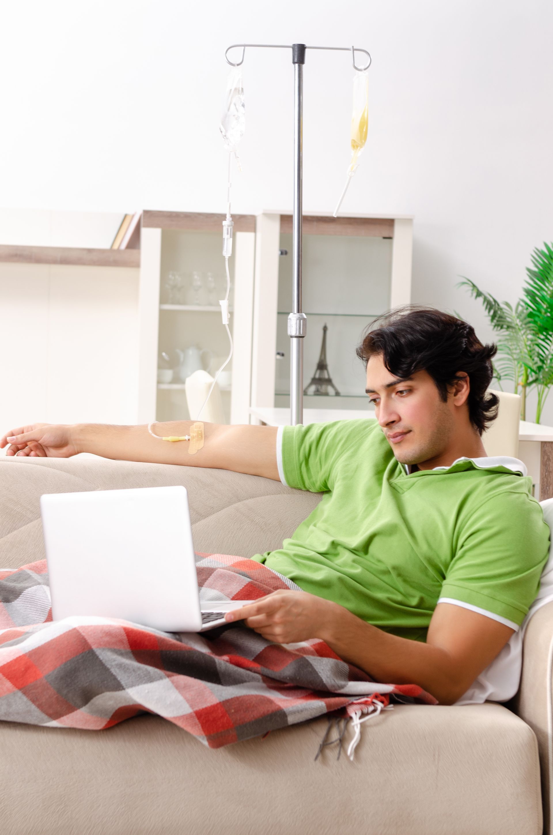 A man is laying on a couch with an iv in his arm and using a laptop.