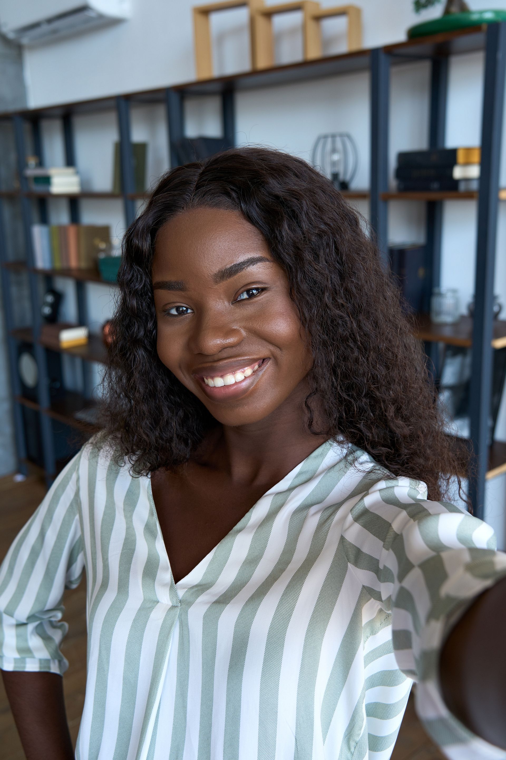 A woman is smiling while taking a selfie in front of a bookshelf.