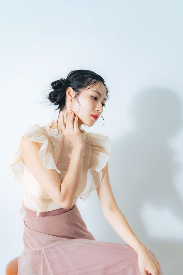 A woman is sitting on a stool with her hands on her face.