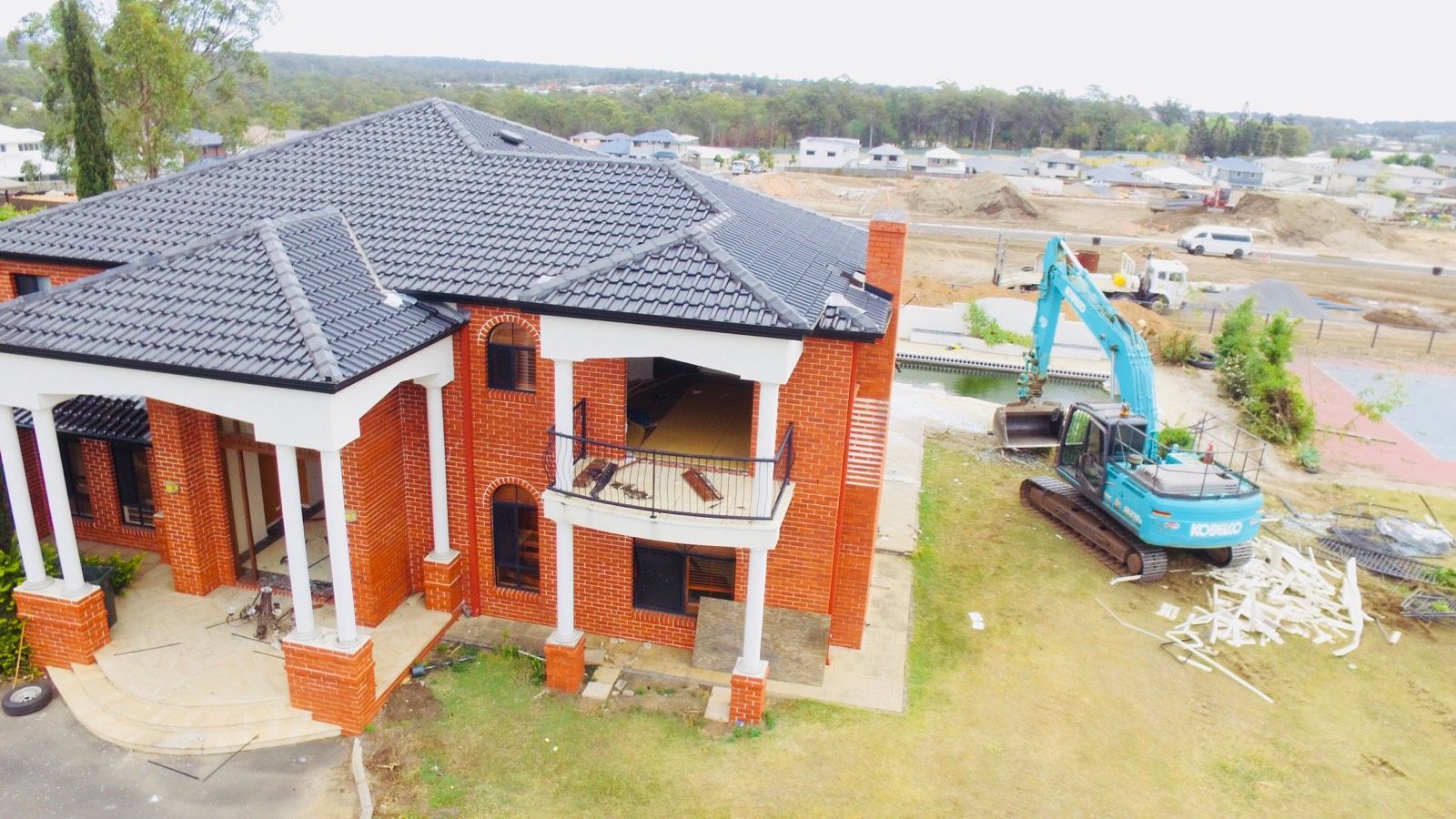 A yellow excavator is demolishing a house behind a fence.