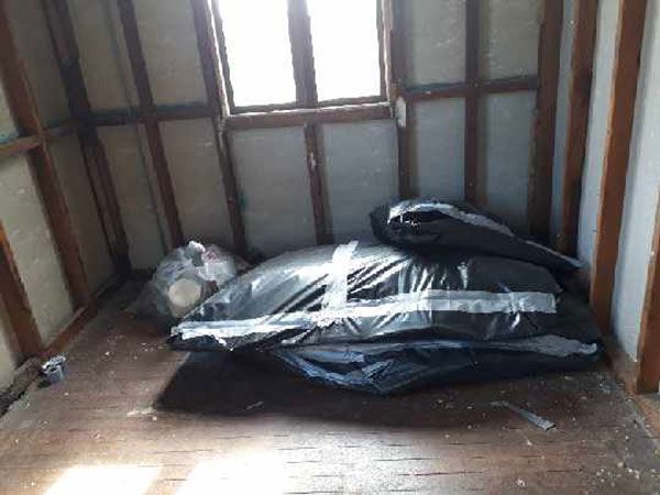 A yellow excavator is demolishing a house behind a fence.