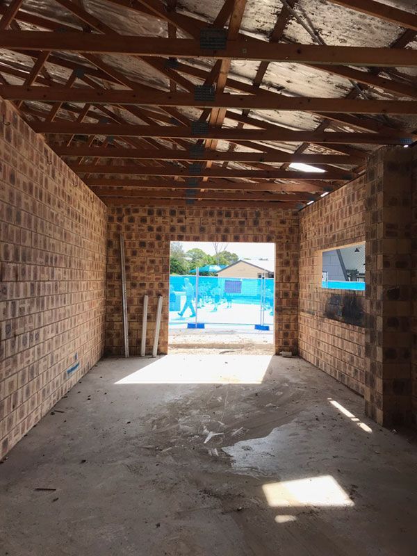 A yellow excavator is demolishing a house behind a fence.
