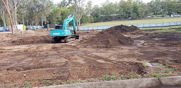 A yellow excavator is demolishing a house behind a fence.