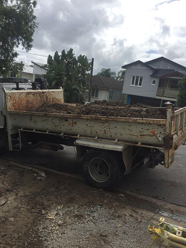 A yellow excavator is demolishing a house behind a fence.