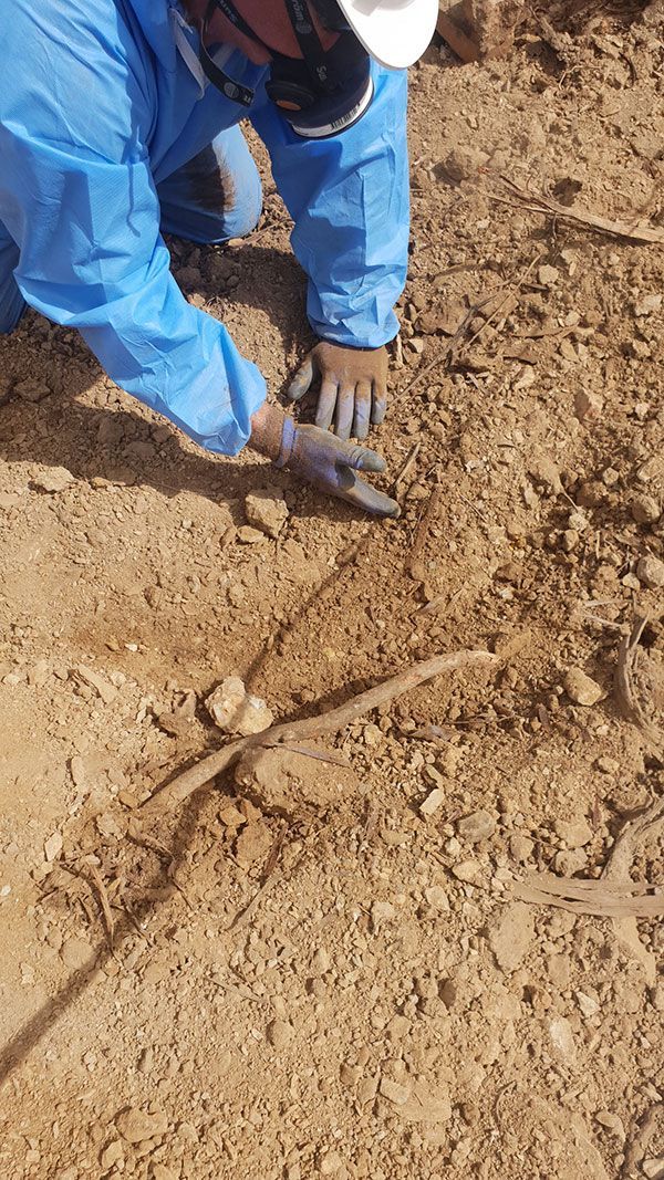A yellow excavator is demolishing a house behind a fence.