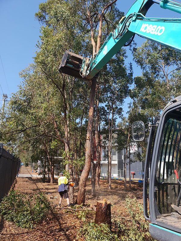 A yellow excavator is demolishing a house behind a fence.