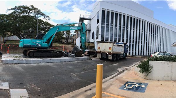 A yellow excavator is demolishing a house behind a fence.