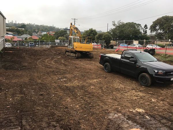 A yellow excavator is demolishing a house behind a fence.