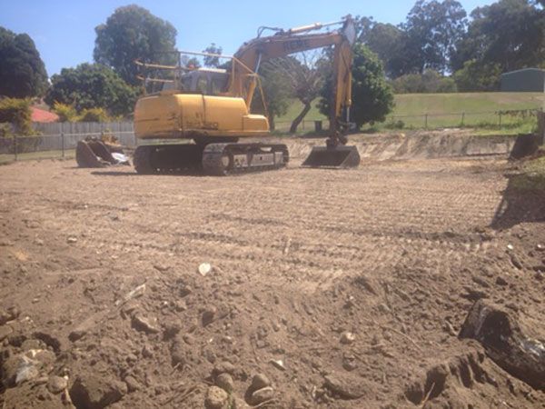 A yellow excavator is demolishing a house behind a fence.