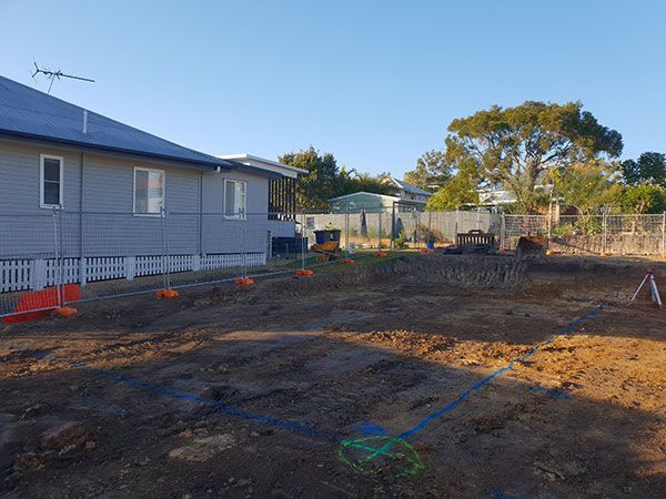 A yellow excavator is demolishing a house behind a fence.
