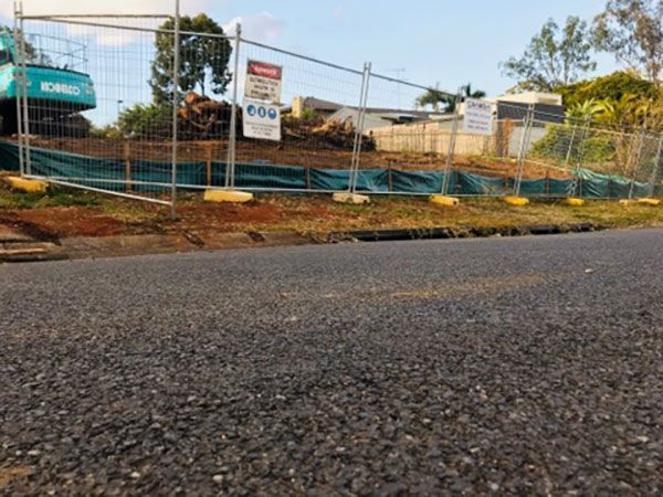 A yellow excavator is demolishing a house behind a fence.