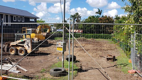 A yellow excavator is demolishing a house behind a fence.