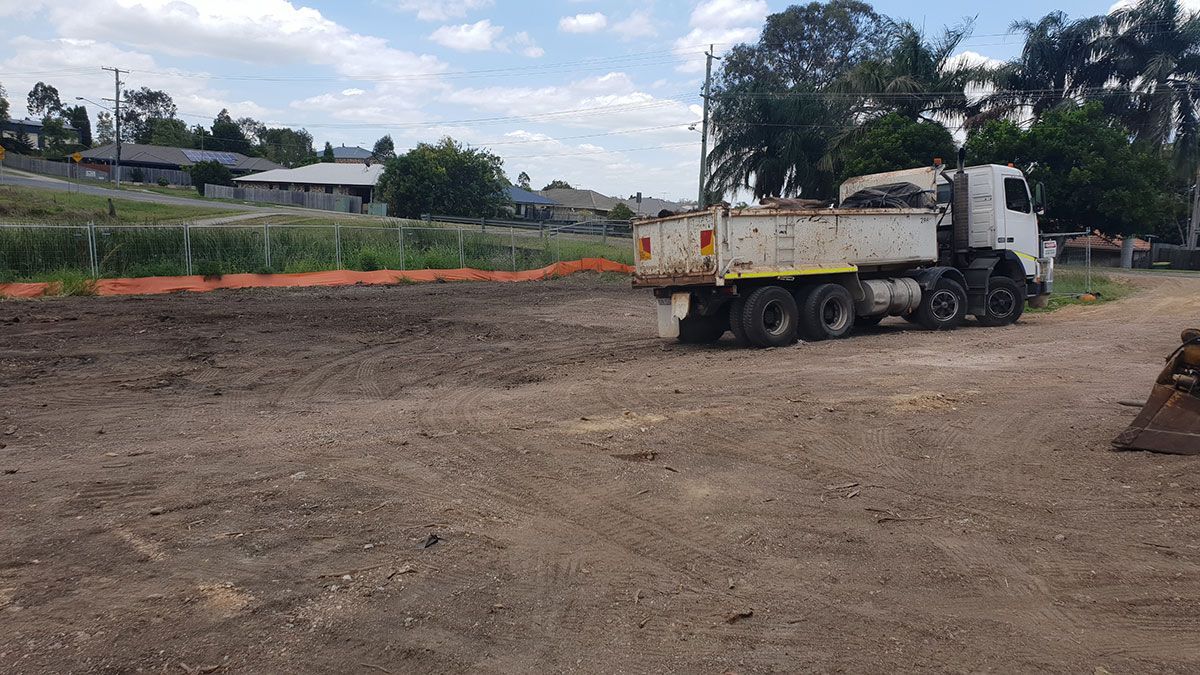 A yellow excavator is demolishing a house behind a fence.