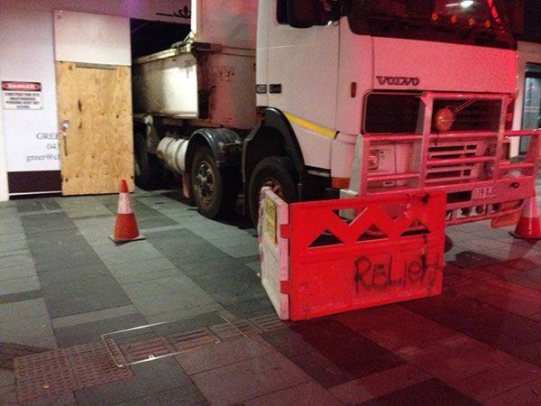 A yellow excavator is demolishing a house behind a fence.