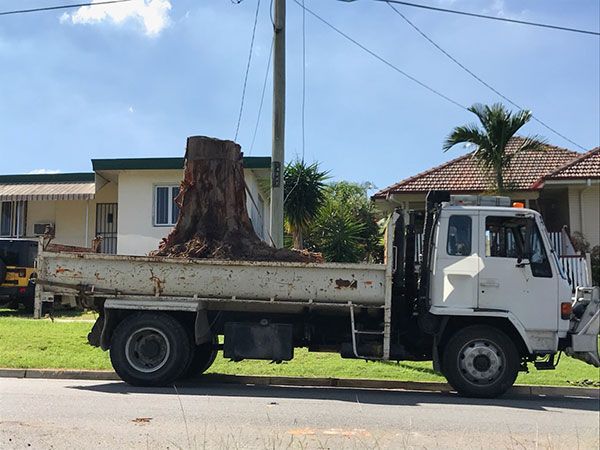 A yellow excavator is demolishing a house behind a fence.