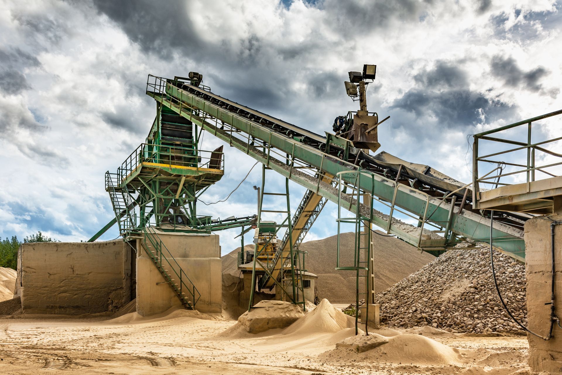 Sand processing plant with conveyor belts and piles of sand against a cloudy sky.