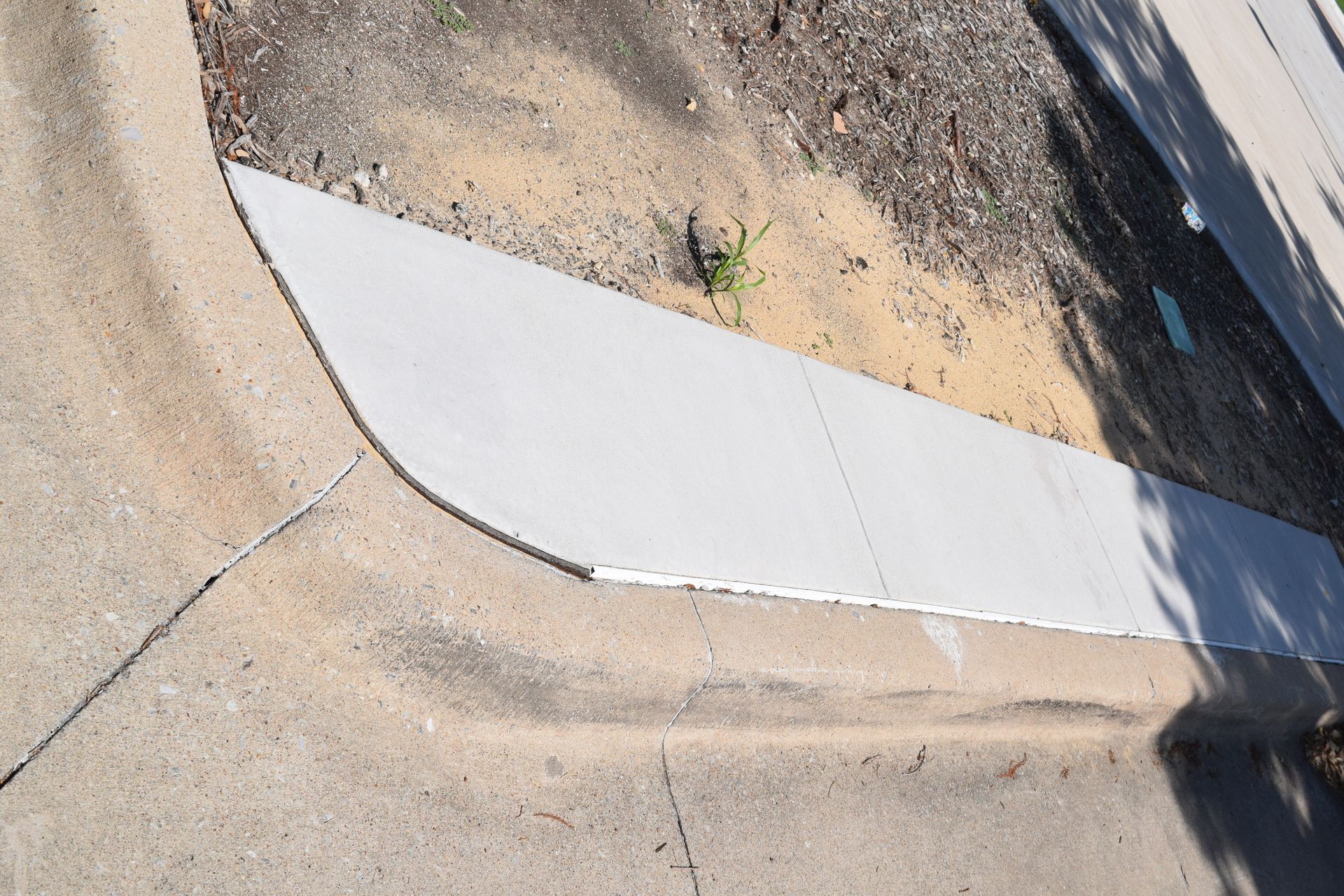 Concrete curb with a sidewalk and a strip of dirt and small plants.