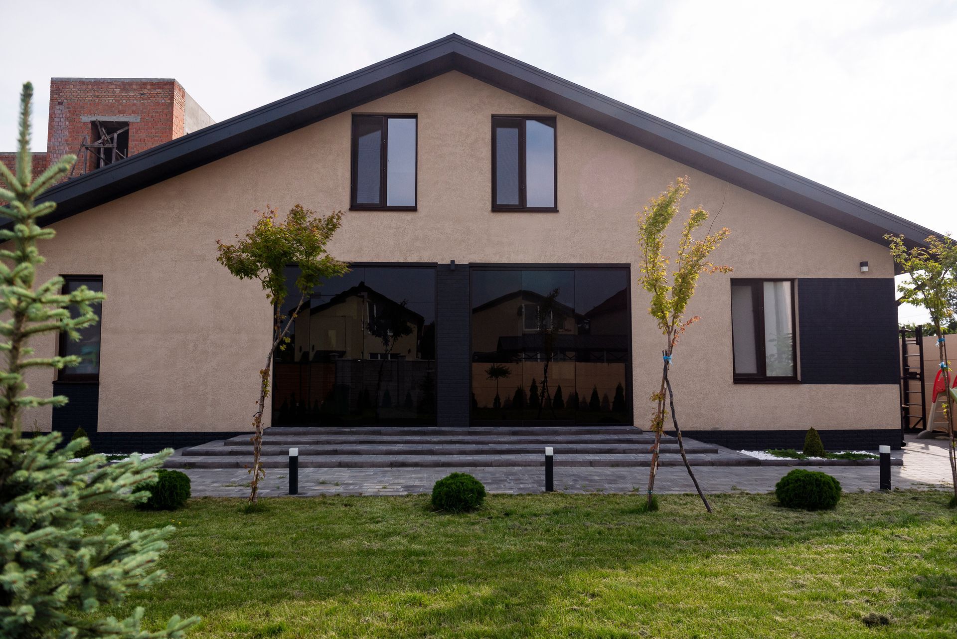 A courtyard of a private one-storey house with tinted windows and doors, a lawn and a playground.