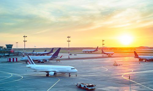 A group of airplanes are parked on a runway at an airport at sunset.