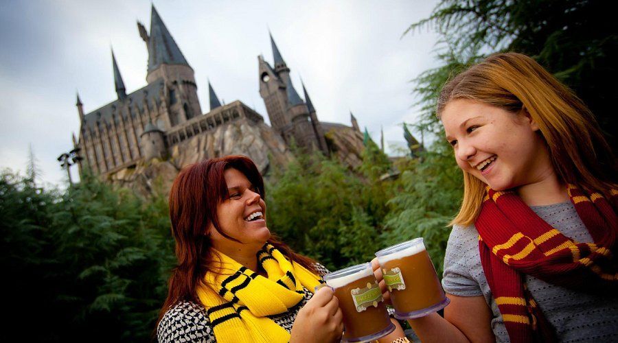 A woman and a girl are holding mugs of beer in front of a castle.