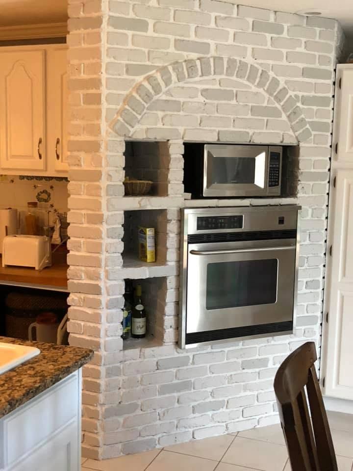 Kitchen wall with arched white brick oven alcove, built-in microwave and oven, and small storage shelves