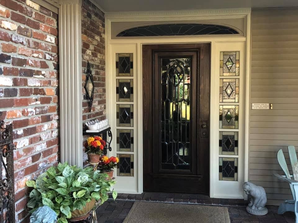 Front porch entry with a black door, sidelights, brick wall, and potted flowers