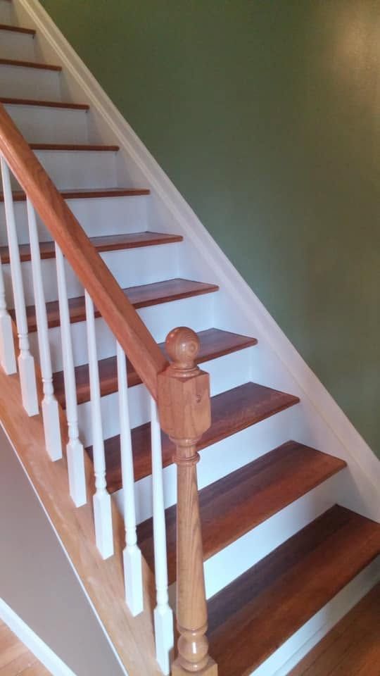 Wooden staircase with white balusters and dark treads against a green wall.