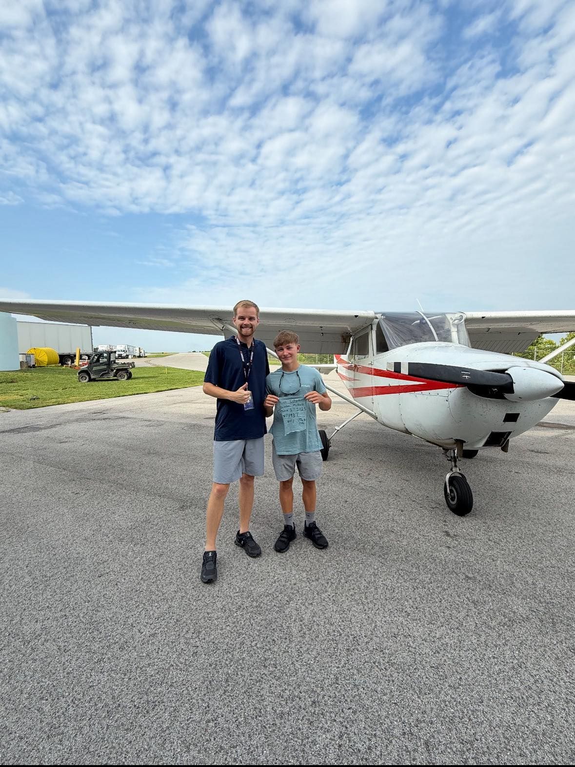 Two men stand by a small plane on a sunny tarmac. One gives a thumbs up.