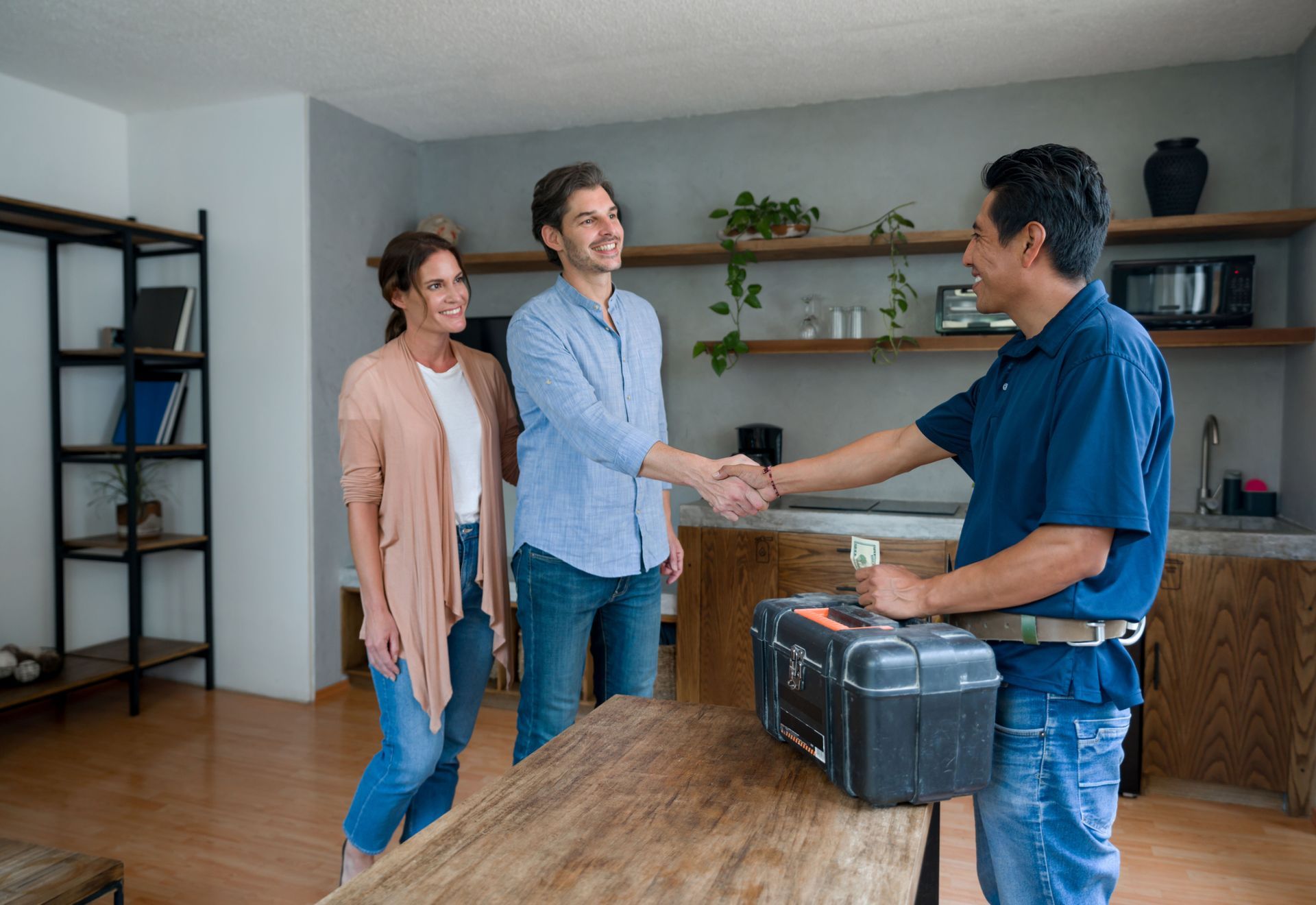 A man and woman are shaking hands with a plumber in a living room.