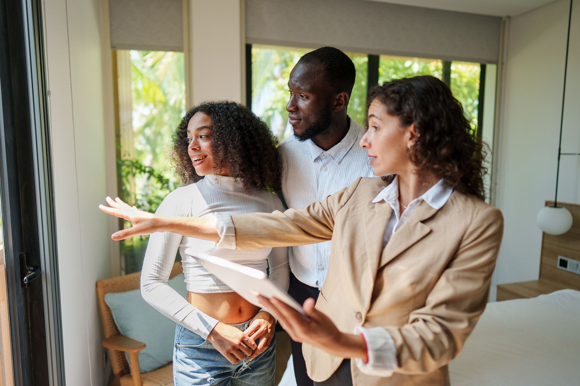 Person with curly hair and glasses smiles widely, wearing a beige sweater with text.