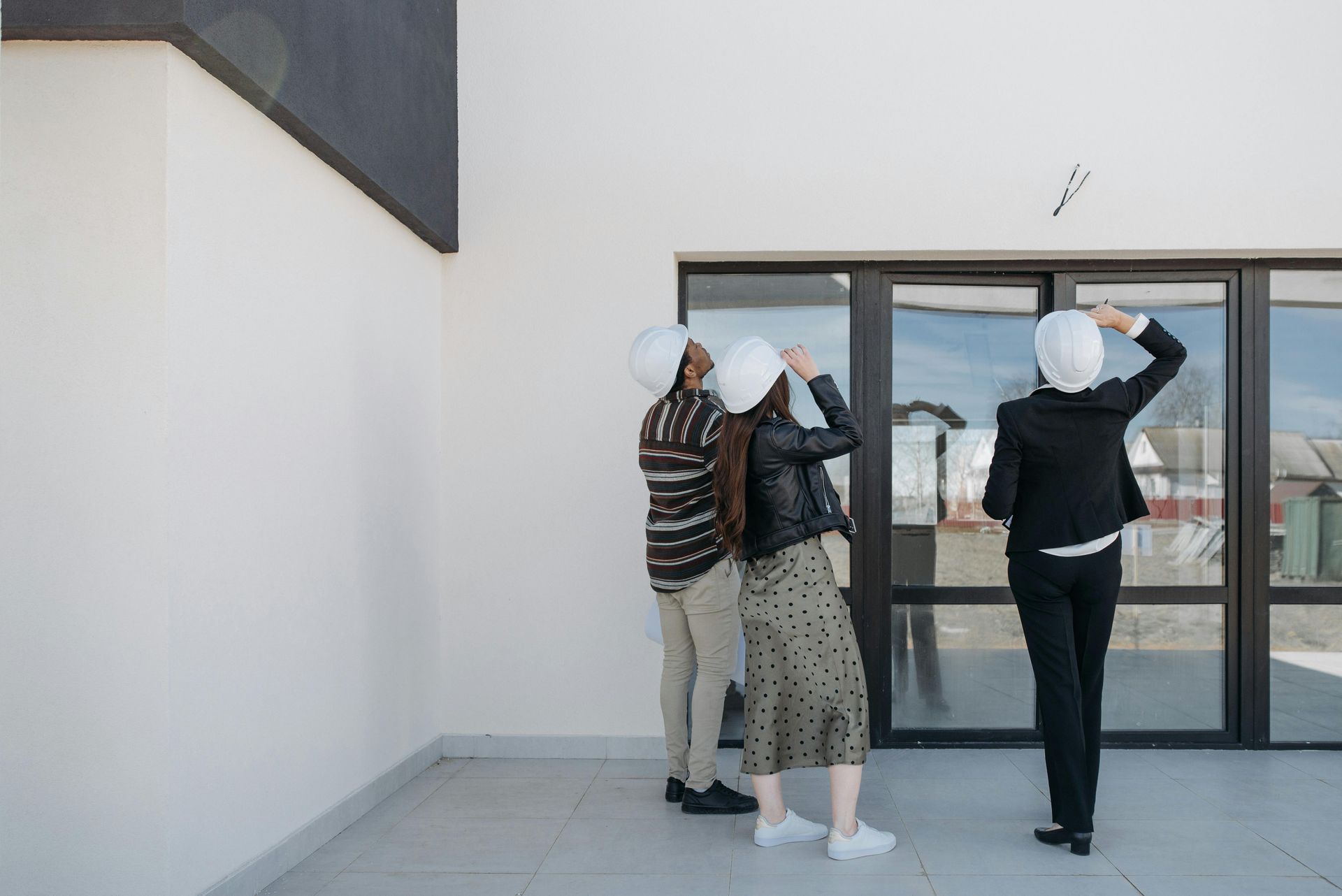 Three people in hard hats looking up at a building exterior; one gestures at it.