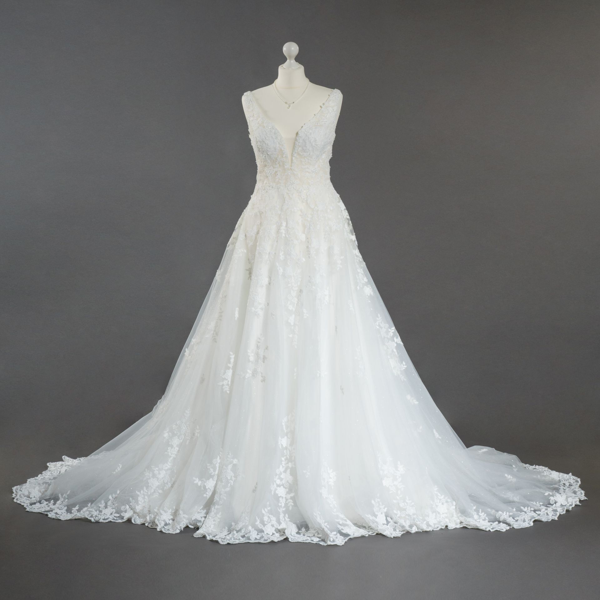 Auf einer Schaufensterpuppe hängt vor einem grauen Hintergrund ein weißes Brautkleid.