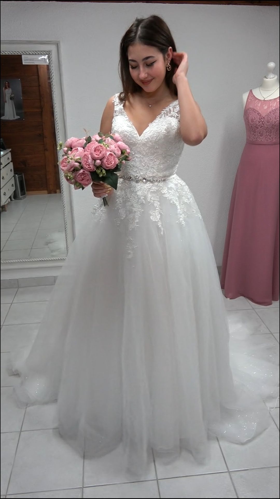 Eine Frau in einem weißen Brautkleid hält einen Strauß rosa Blumen in der Hand.