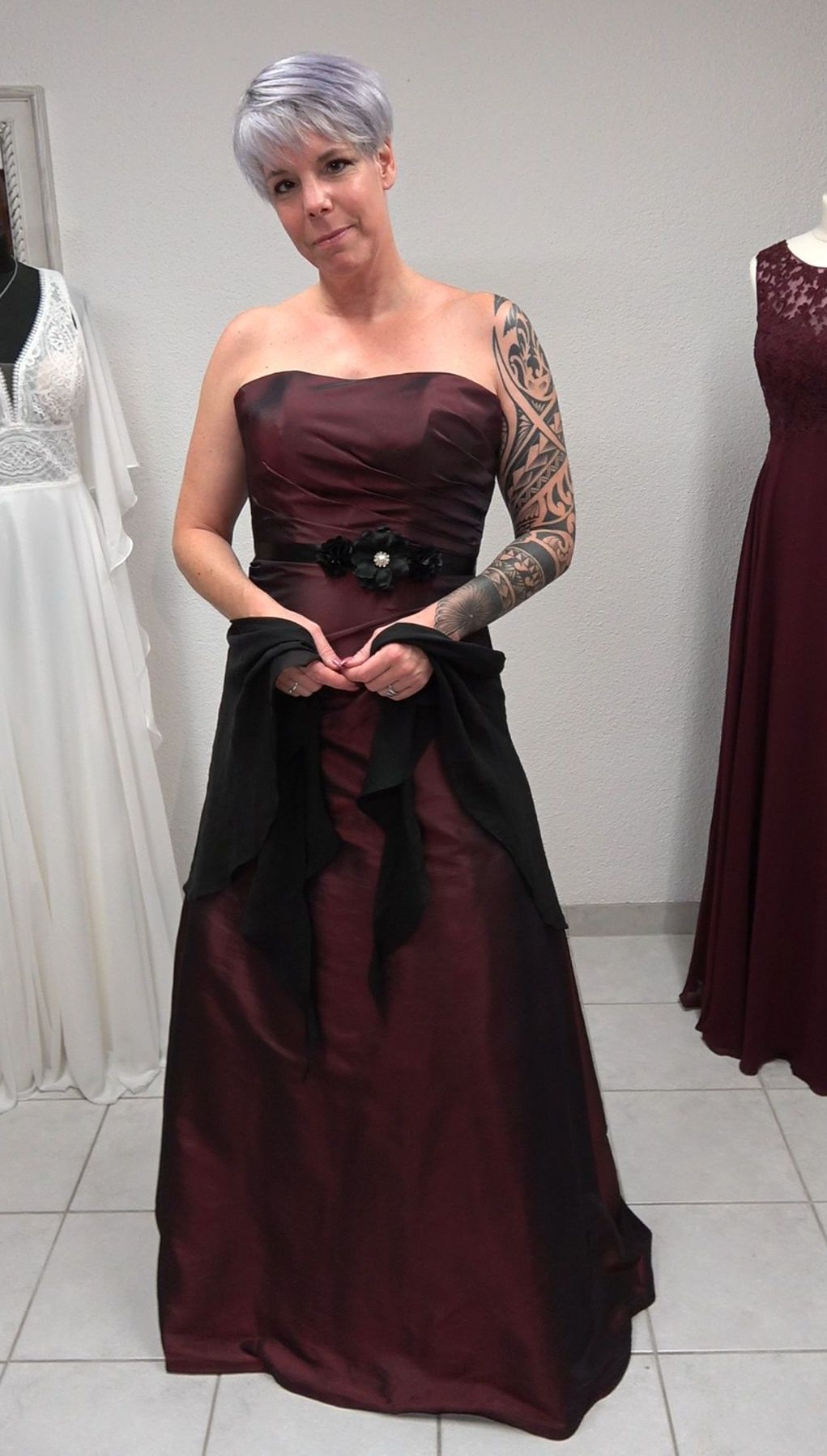 Eine Frau mit einer Tätowierung auf dem Arm trägt ein burgunderrotes und schwarzes Kleid.