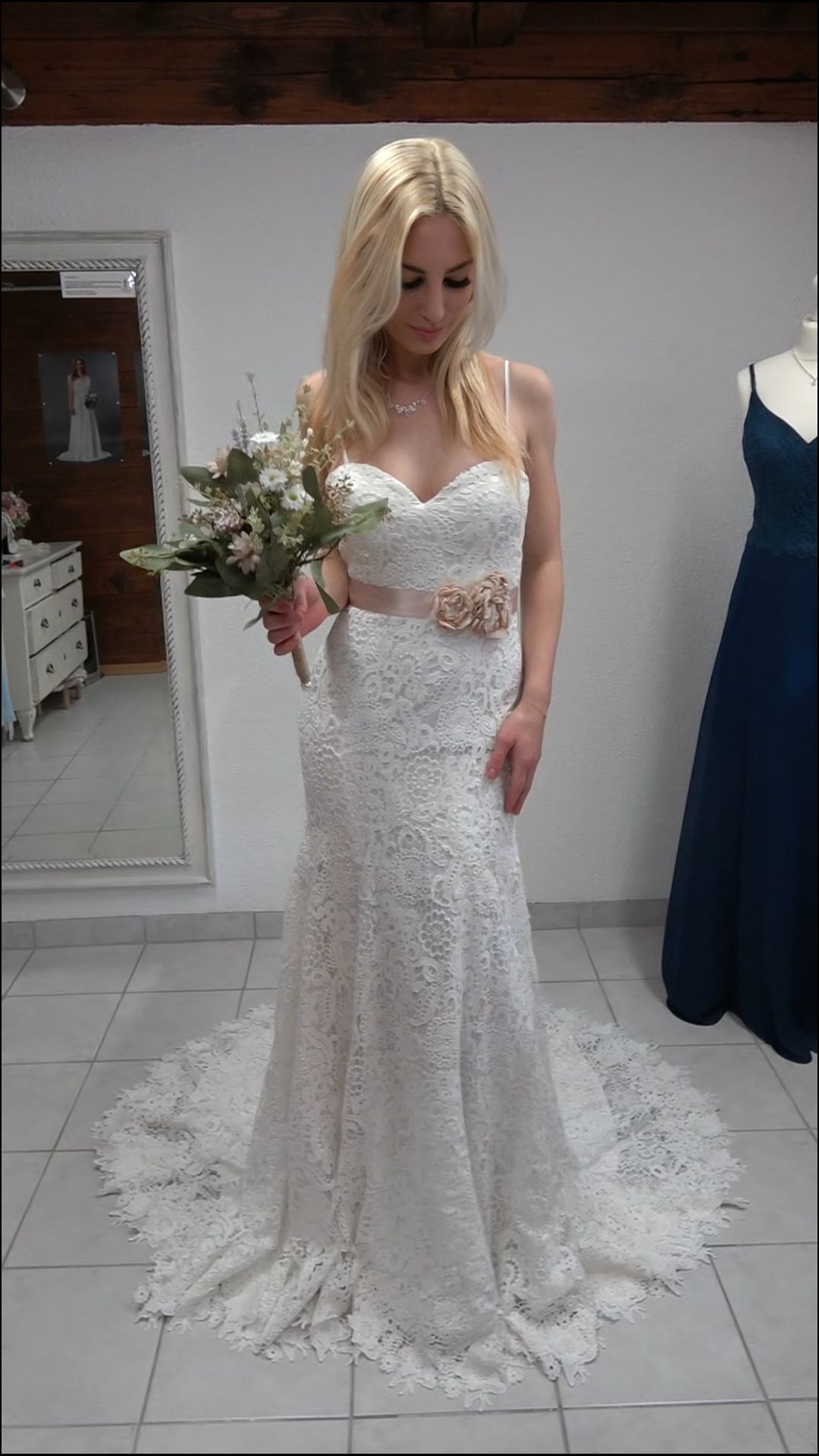 Eine Frau in einem weißen Spitzenbrautkleid hält einen Blumenstrauß.