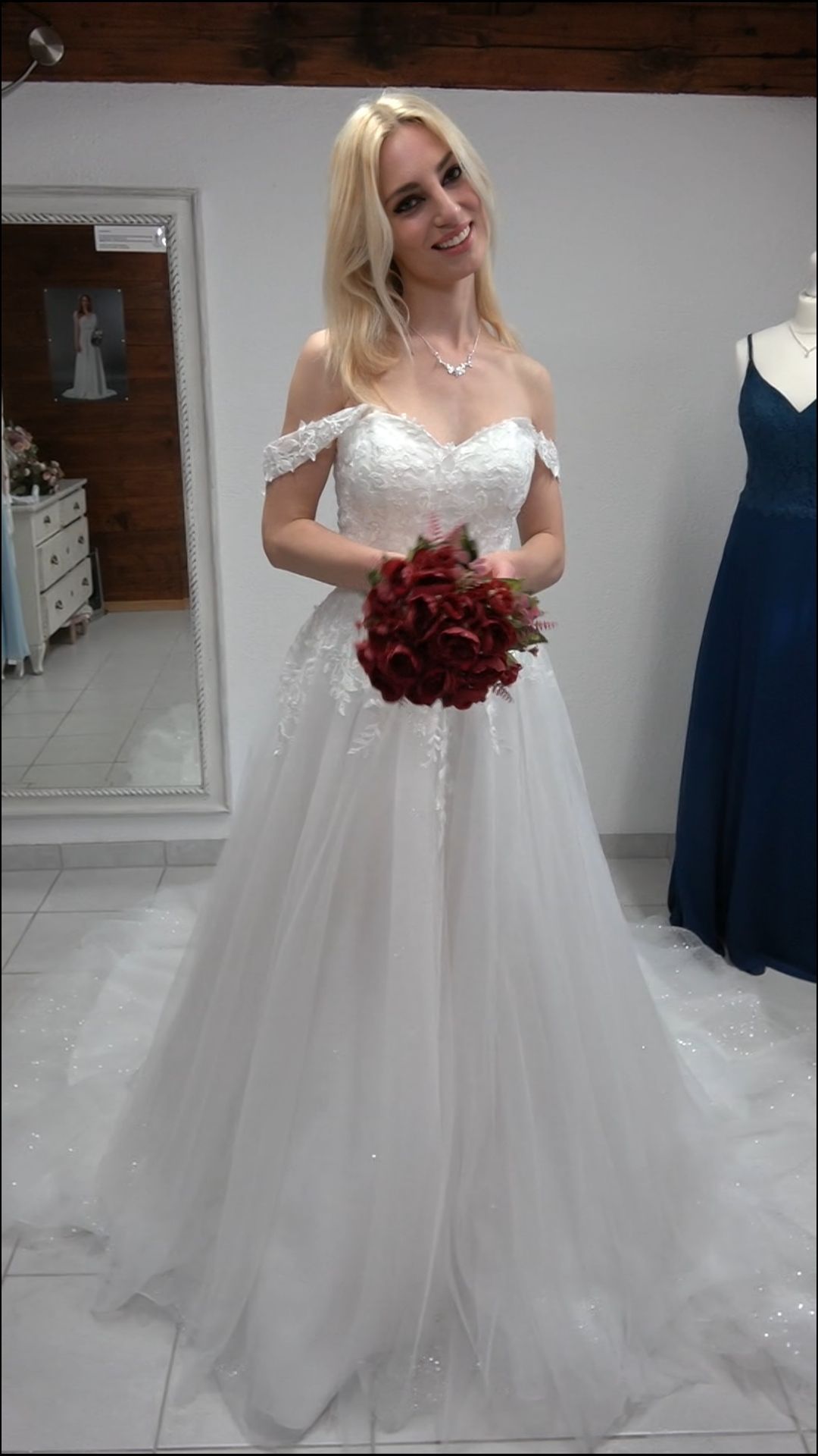 Eine Frau in einem weißen Brautkleid hält einen Strauß roter Rosen in der Hand.