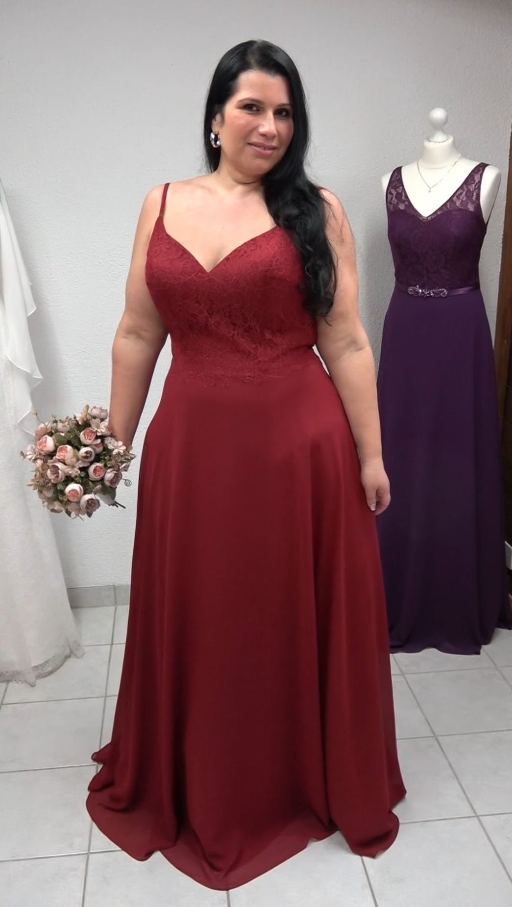 Eine Frau trägt ein langes rotes Kleid und hält einen Blumenstrauß in der Hand.