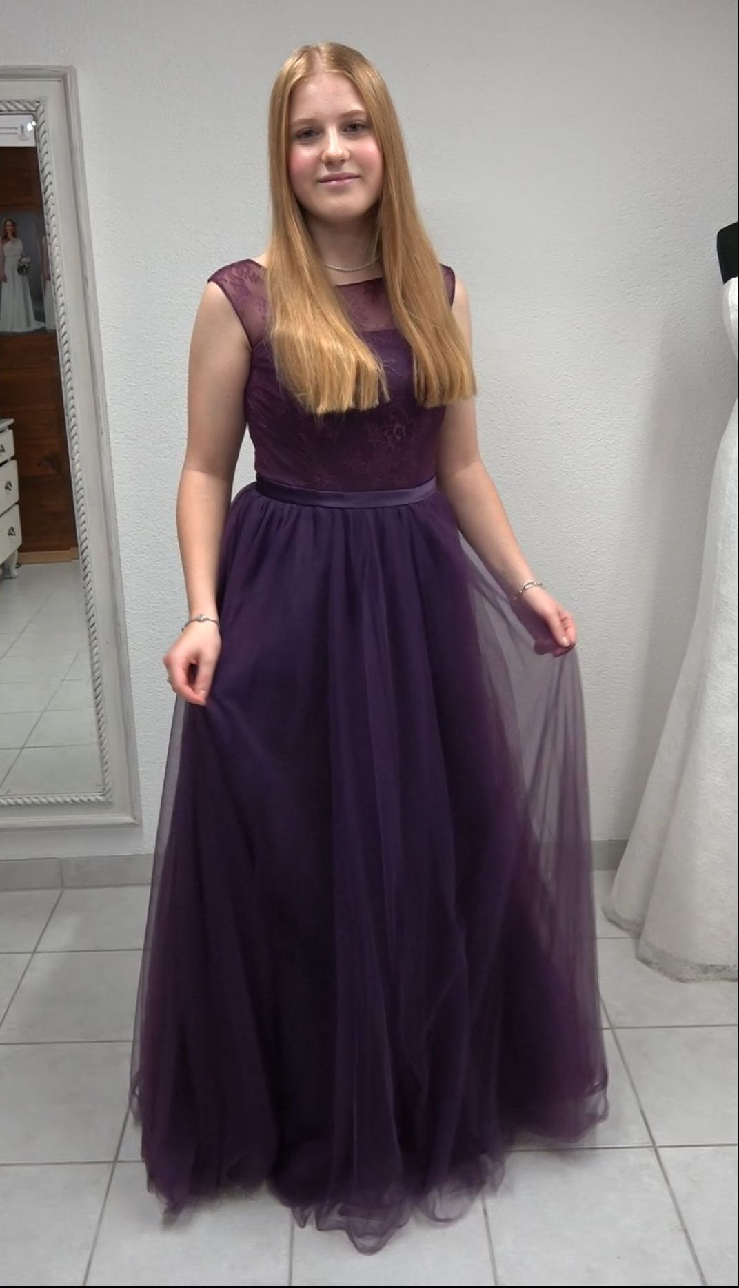 Eine Frau in einem lila Kleid steht vor einem Spiegel.