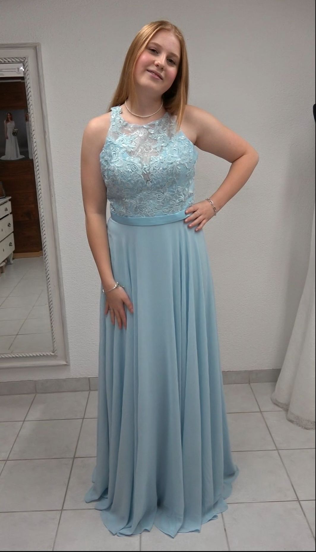 Eine Frau in einem hellblauen Kleid steht vor einem Spiegel.