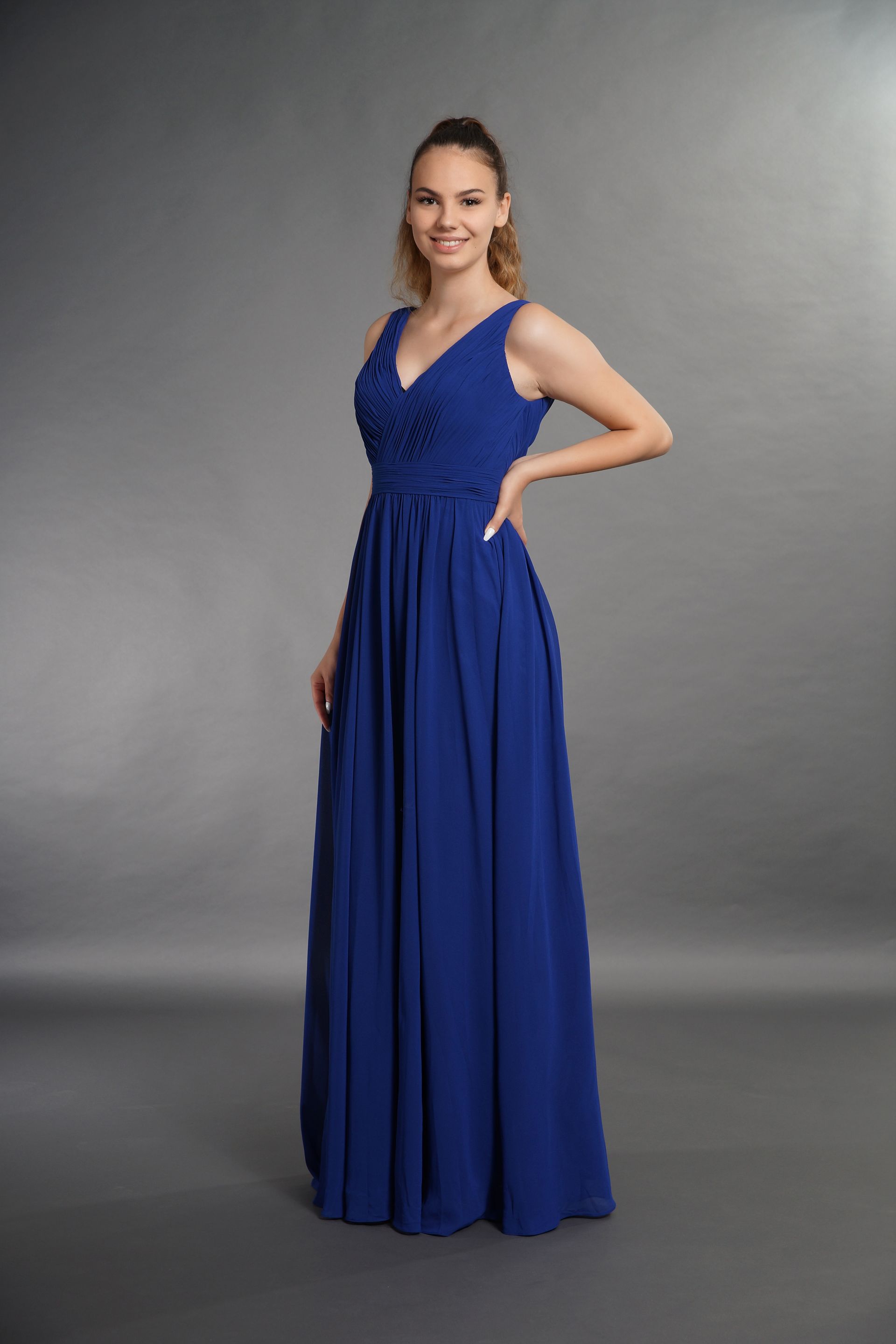 Eine Frau in einem langen blauen Kleid steht vor einem grauen Hintergrund.