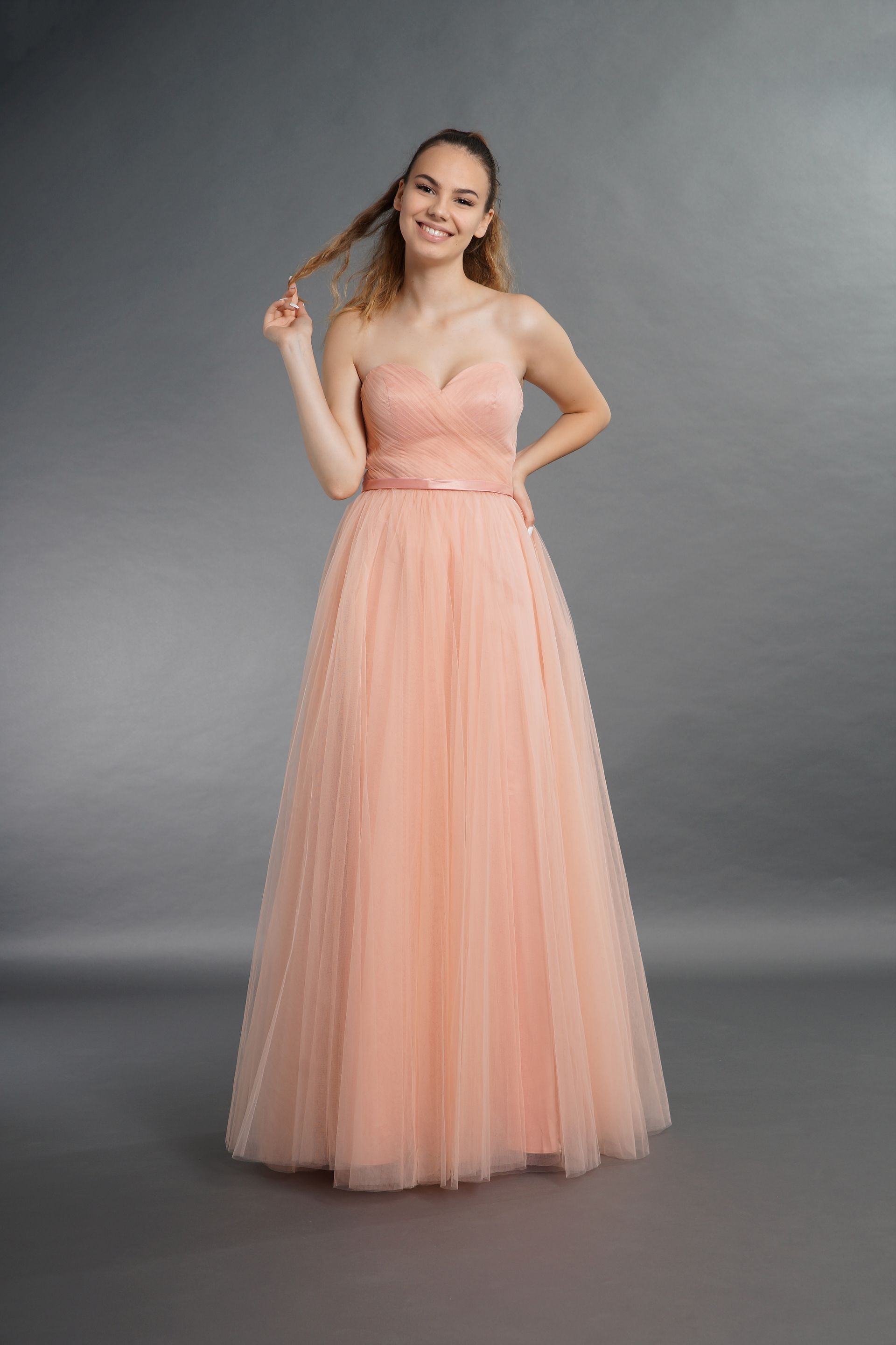 Eine Frau in einem langen rosa Kleid steht vor einem grauen Hintergrund.