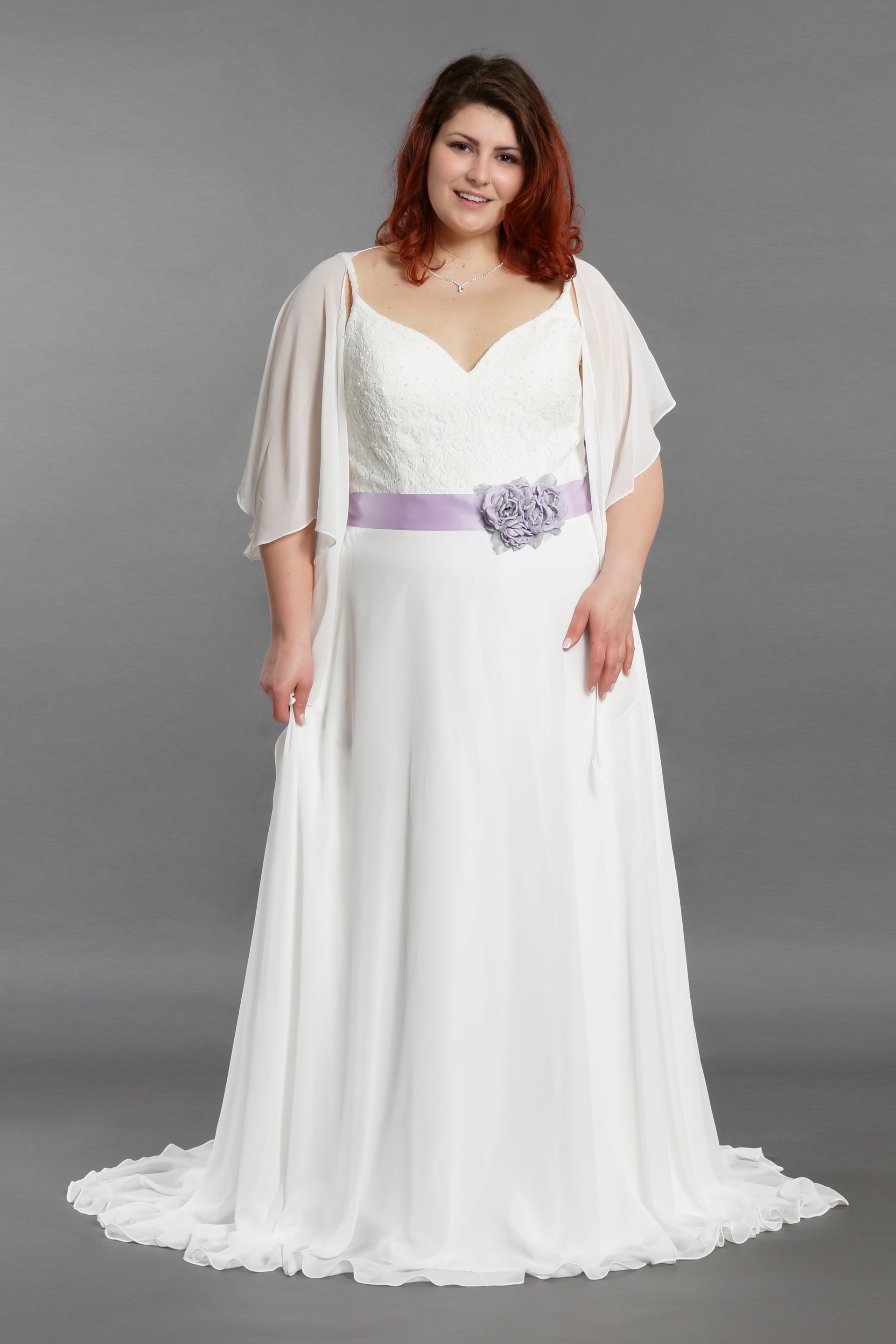 Eine Frau mit Übergröße trägt ein weißes Brautkleid mit einem lila Gürtel.