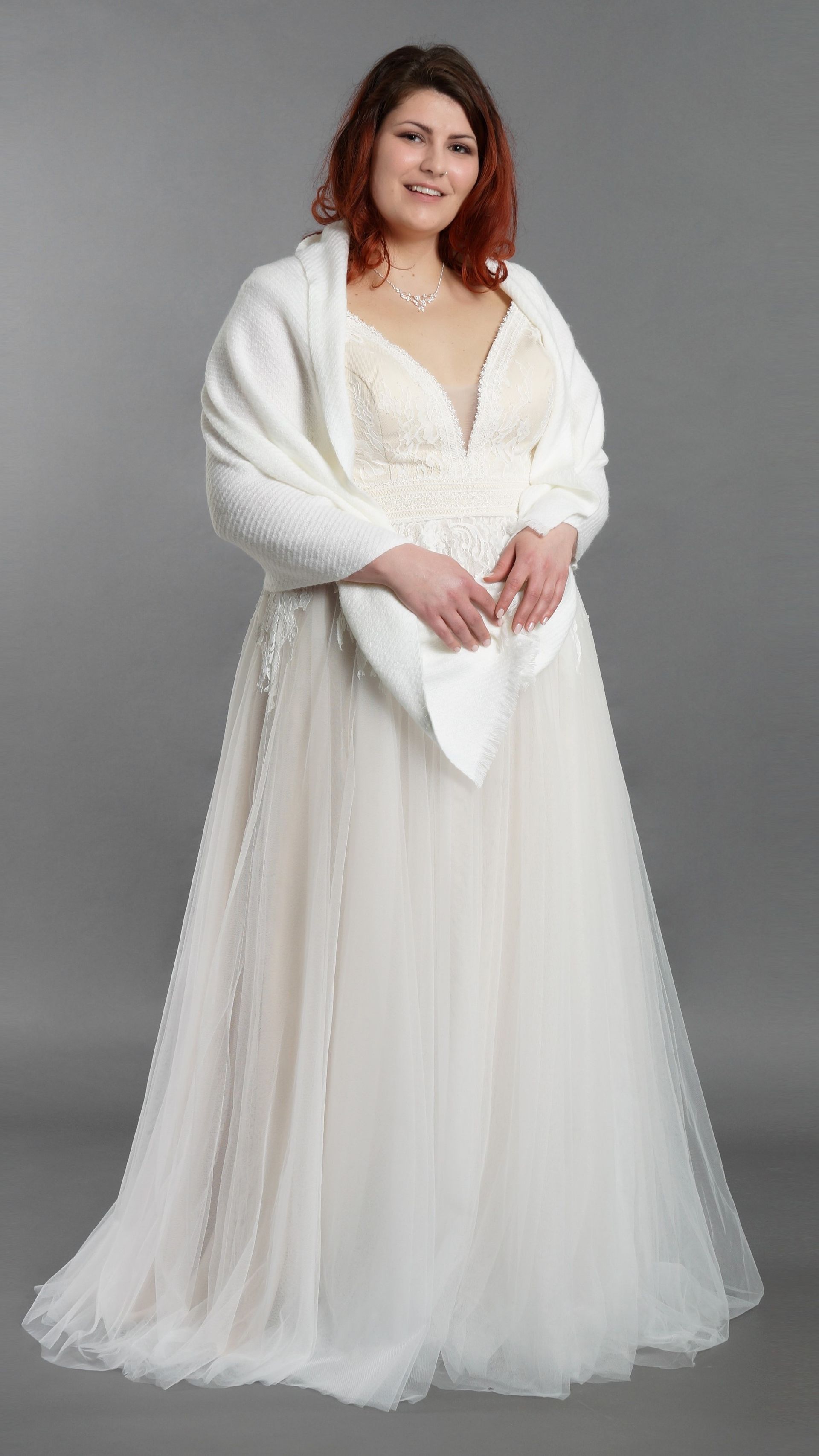 Eine Frau in einem weißen Brautkleid trägt einen weißen Schal.