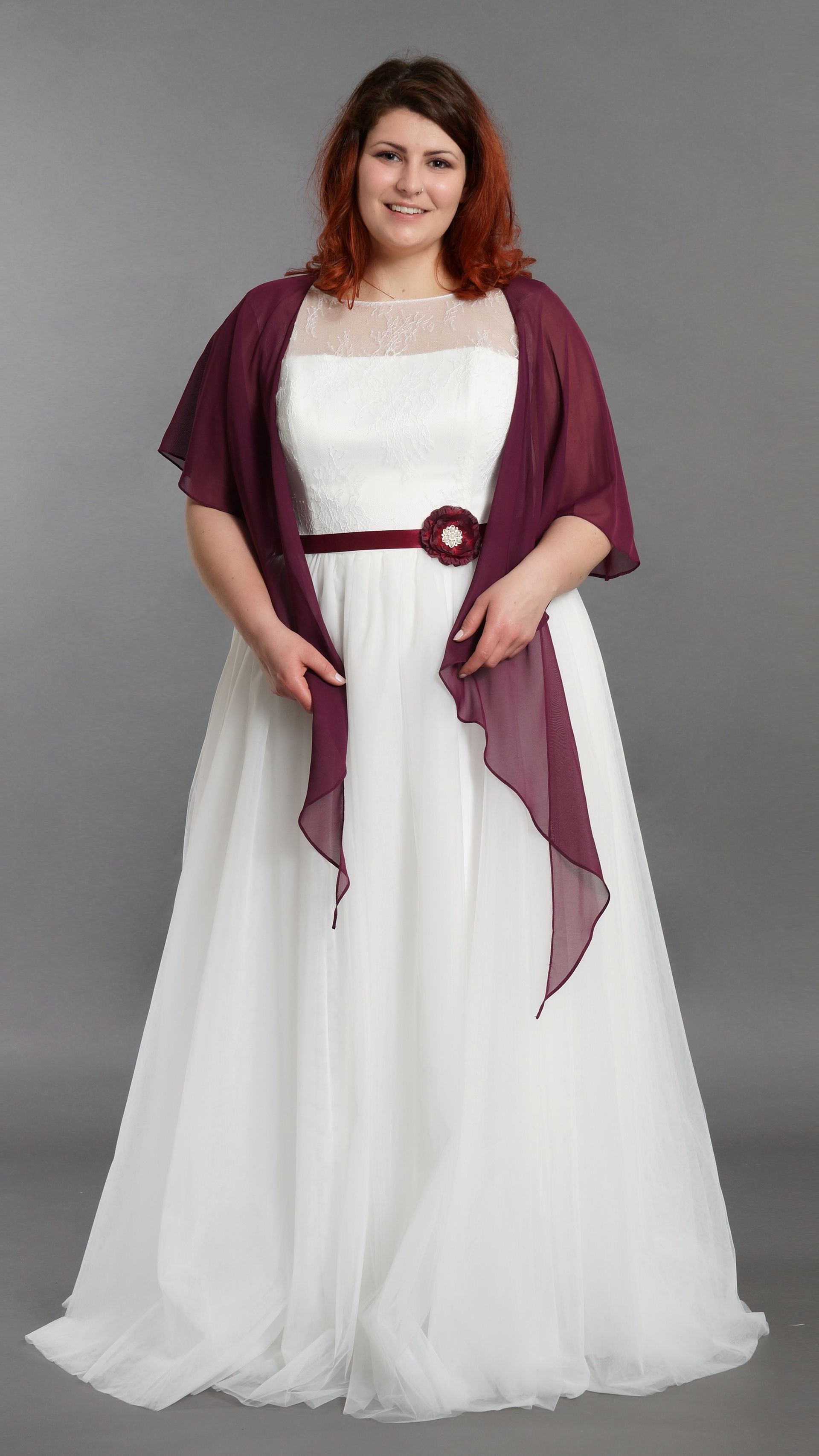 Eine Frau mit Übergröße trägt ein weißes Kleid und einen weinroten Schal.