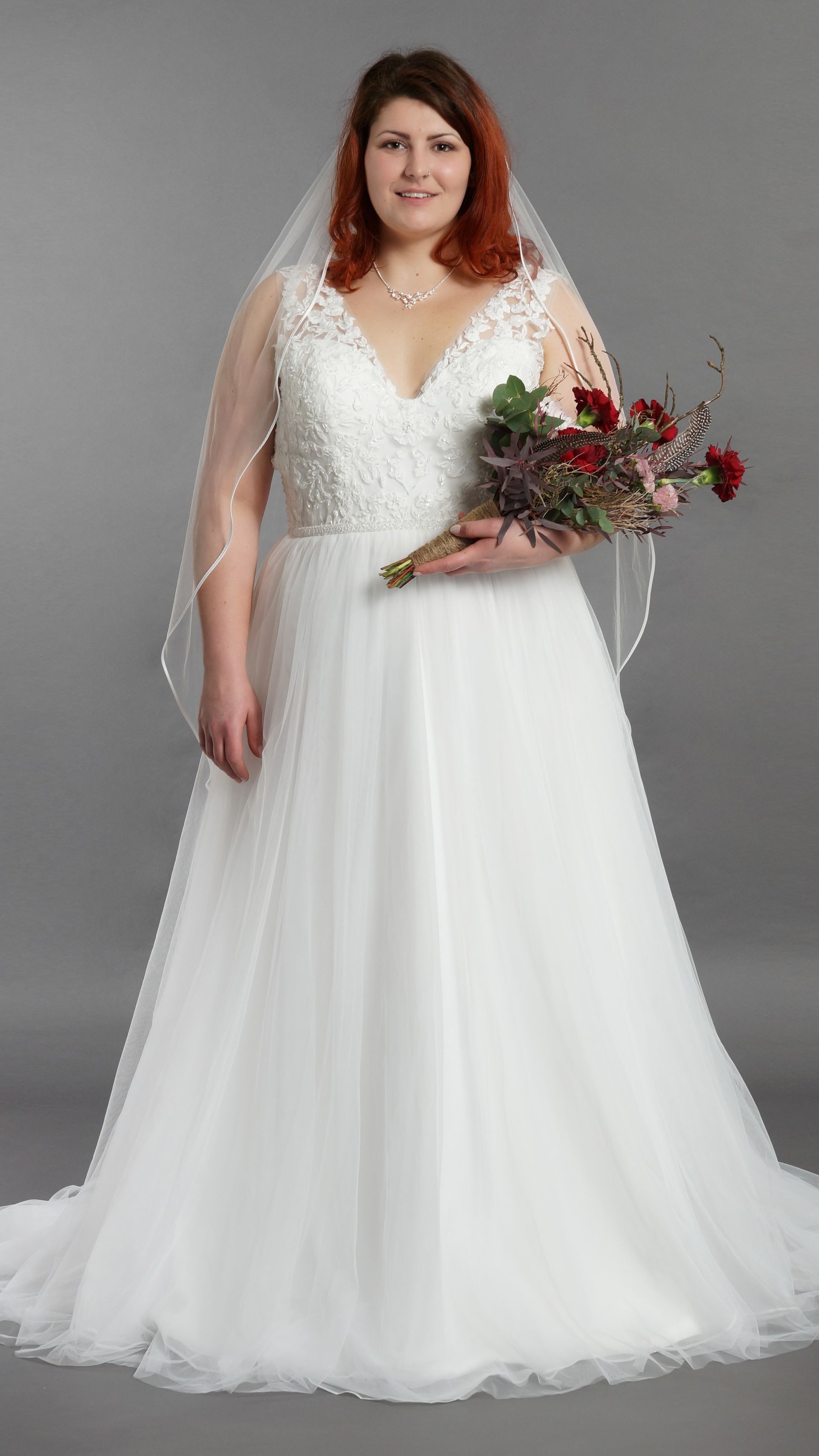 Eine Braut in Übergröße in einem weißen Brautkleid und Schleier hält einen Blumenstrauß.